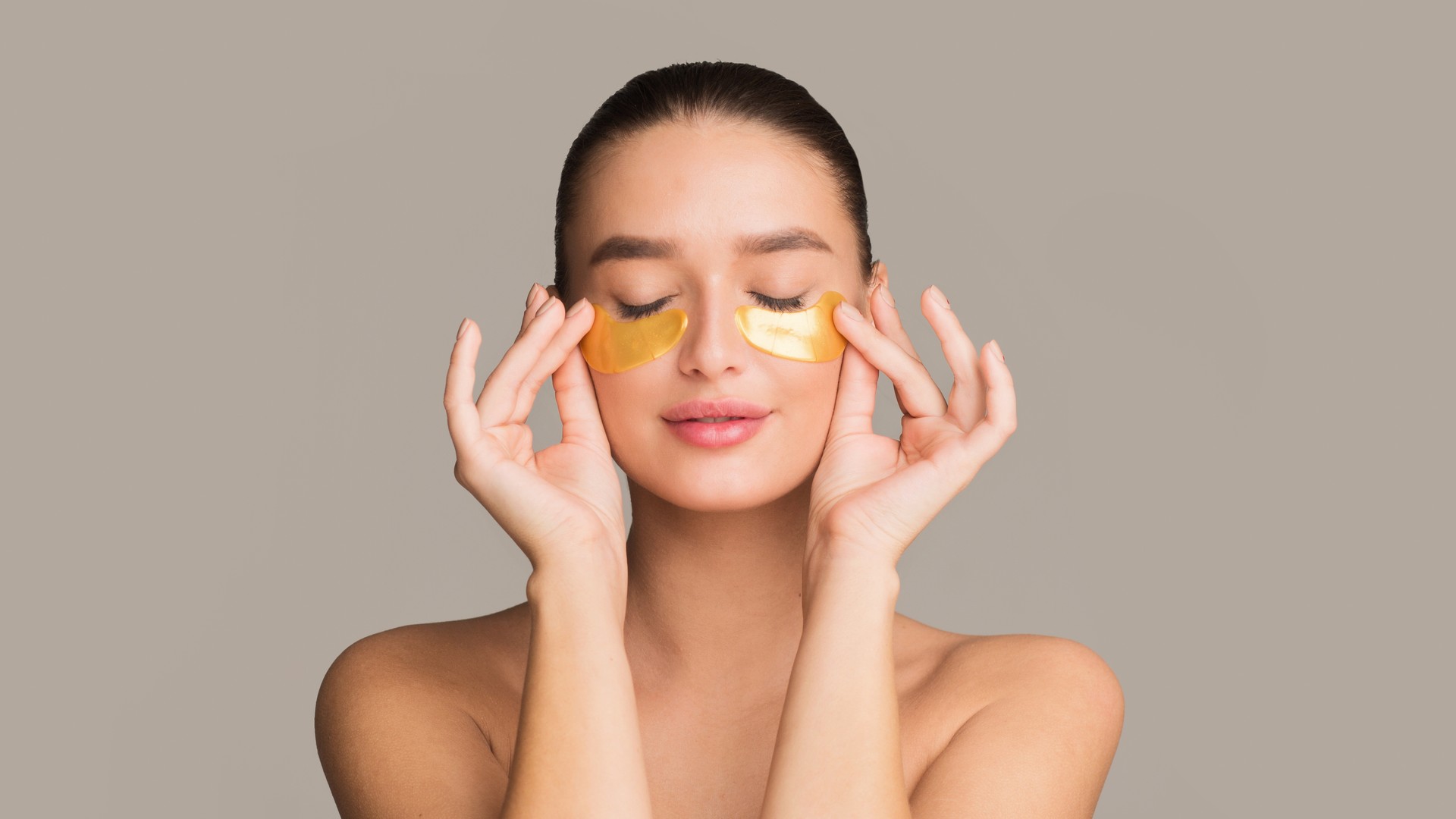 Young woman applying golden collagen patches under eyes